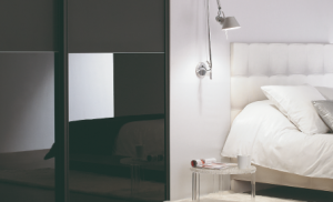 façade de placard noir avec vitre laquée noire et à sa droite un lit avec parure et tête de lit blanc